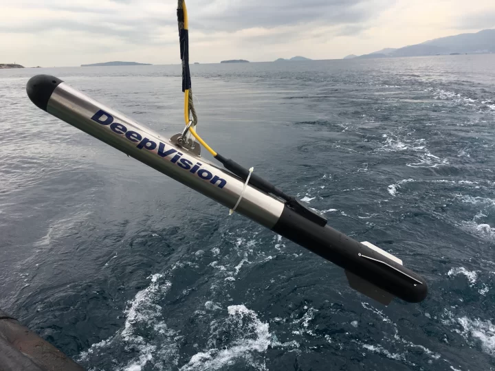 DeepVision side-scan sonar towfish suspended above the sea beside a survey vessel